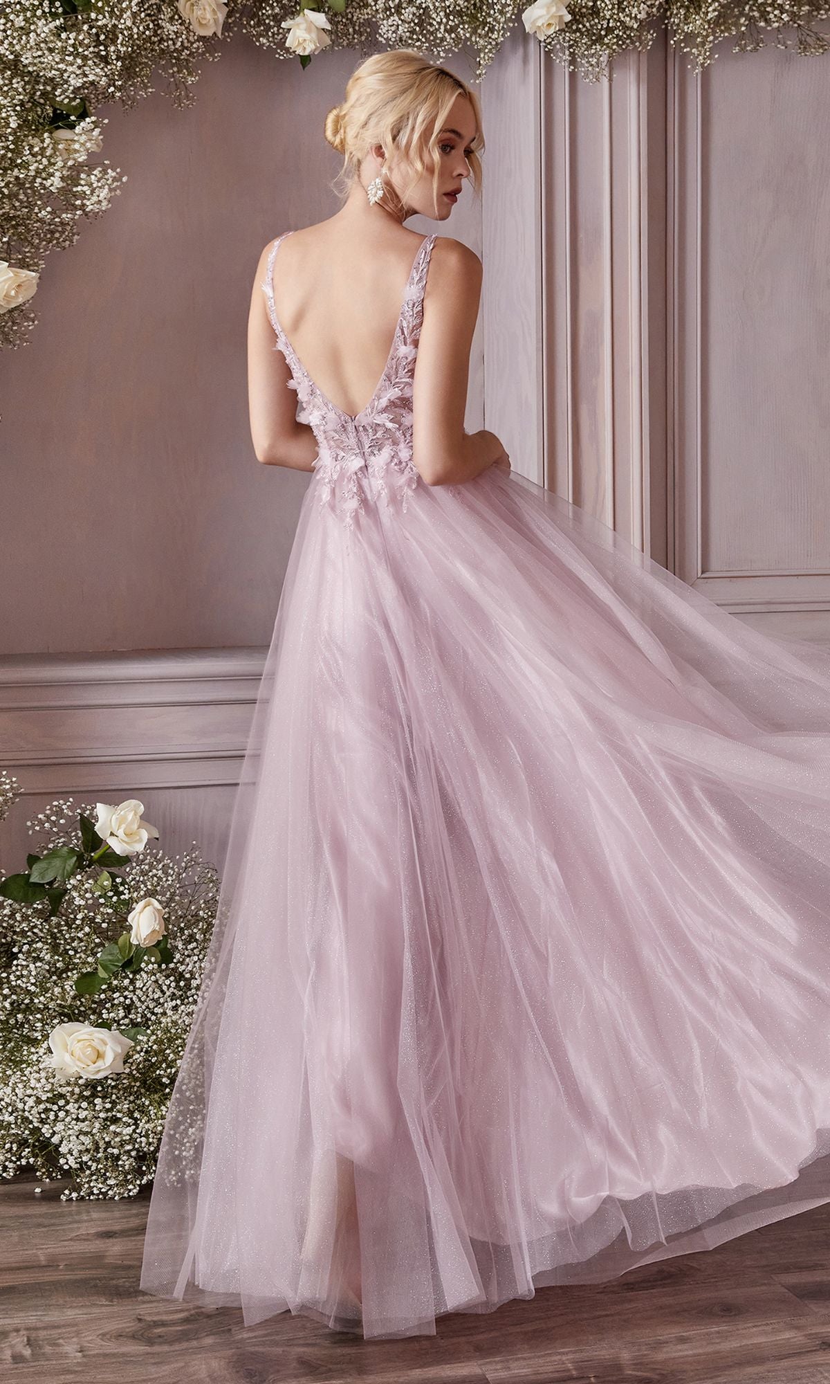 A woman wearing the Ladivine CD0181 Glitter Tulle Illusion Prom Dress with a low back stands in a room decorated with white roses and baby's breath flowers.